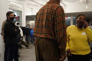 The poll site manager at Huntington Hall waits on hold as she calls to get the ballot printer fixed. Meanwhile, voters wait in line for their ballots.